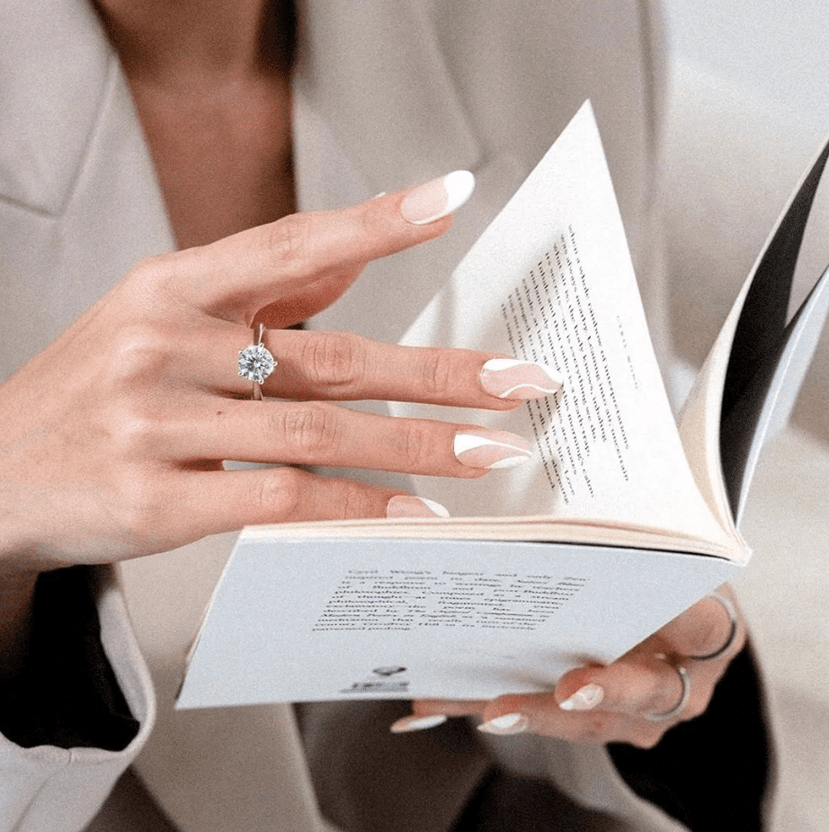 a woman reading a book while wearing a solitaire engagement ring