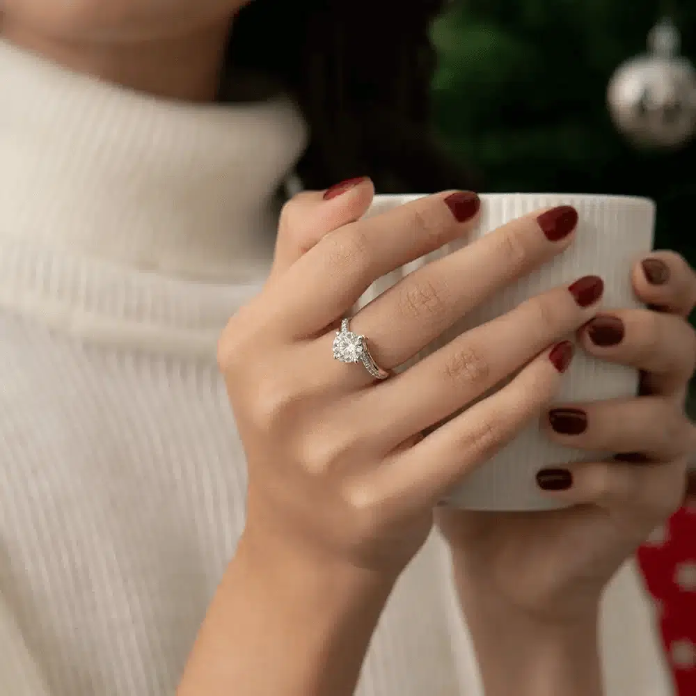 SK a woman wearing a rose gold diamond ring with a twirl shaped pave band in 18k white gold and rose gold and 101 facets lab grown diamond on her middle finger while holding a cup